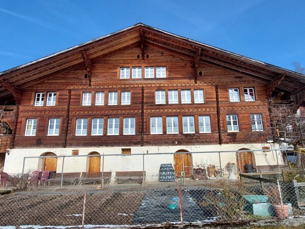 Un grand bâtiment en bois, doté de nombreuses fenêtres et portes, entouré d’une clôture et de divers matériaux de construction.