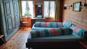Una habitación acogedora con cama, escritorio y silla. Hay ventanas con cortinas, una pared de madera y un ventilador de techo.