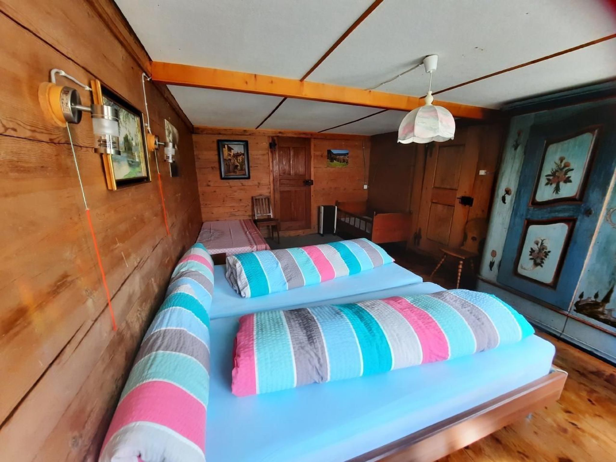 Una habitación acogedora con paredes de madera, una cama con ropa de cama a rayas, una mesita pequeña y una silla.