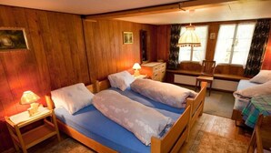 Una habitación de madera con una cama grande, dos mesitas de noche, un aparador y una silla.