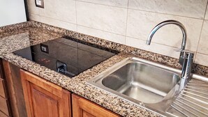 A kitchen with a built-in stove, a sink, wooden cabinets, and a tiled backsplash. - Appartamento con vista sull'acqua by Interhome (Capoliveri)