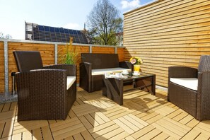 Eine Terrasss mit Korbmöbeln, einem Tisch mit Blumenvase und einer Holzwand.