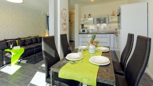 Zona pranzo moderna con tavolo imbandito per quattro persone, un divano e una cucina sullo sfondo.