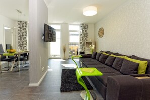 Ein modernes Wohnzimmer mit Sofa, Fernseher, Essbereich und einer Treppe zu einer oberen Etage.