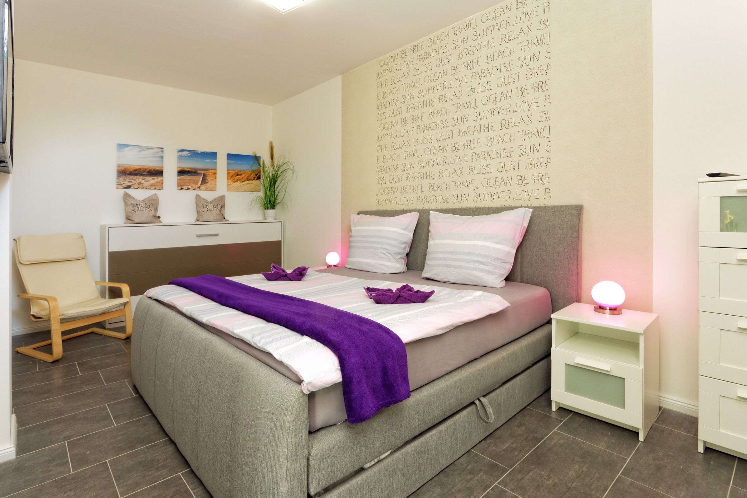 A bedroom with a bed, a chair, a nightstand, a dresser, and a wall with text.