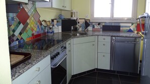 Een keuken met witte kastjes, een granieten aanrecht, een vaatwasser en een raam met zonwering.
