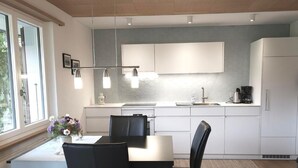 A modern kitchen with white cabinets, a dining table with chairs, and pendant lighting. - Chalet Alouette by Interhome (Aeschi bei Spiez)