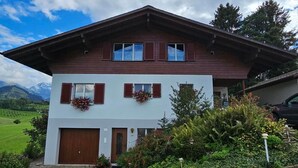 A two-story chalet with a wooden facade, a front garage, and a well-maintained garden with flowering plants. - Chalet Alouette by Interhome (Aeschi bei Spiez)