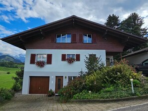 Ein zweigeschossiges Chalet mit Holzfassade, einer Garage und einem gepflegten Garten mit blühenden Pflanzen.