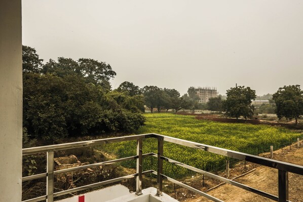 A balcony with a metal railing overlooking a green field and trees. - Hotel The Viraj Palace (Ayodhya)