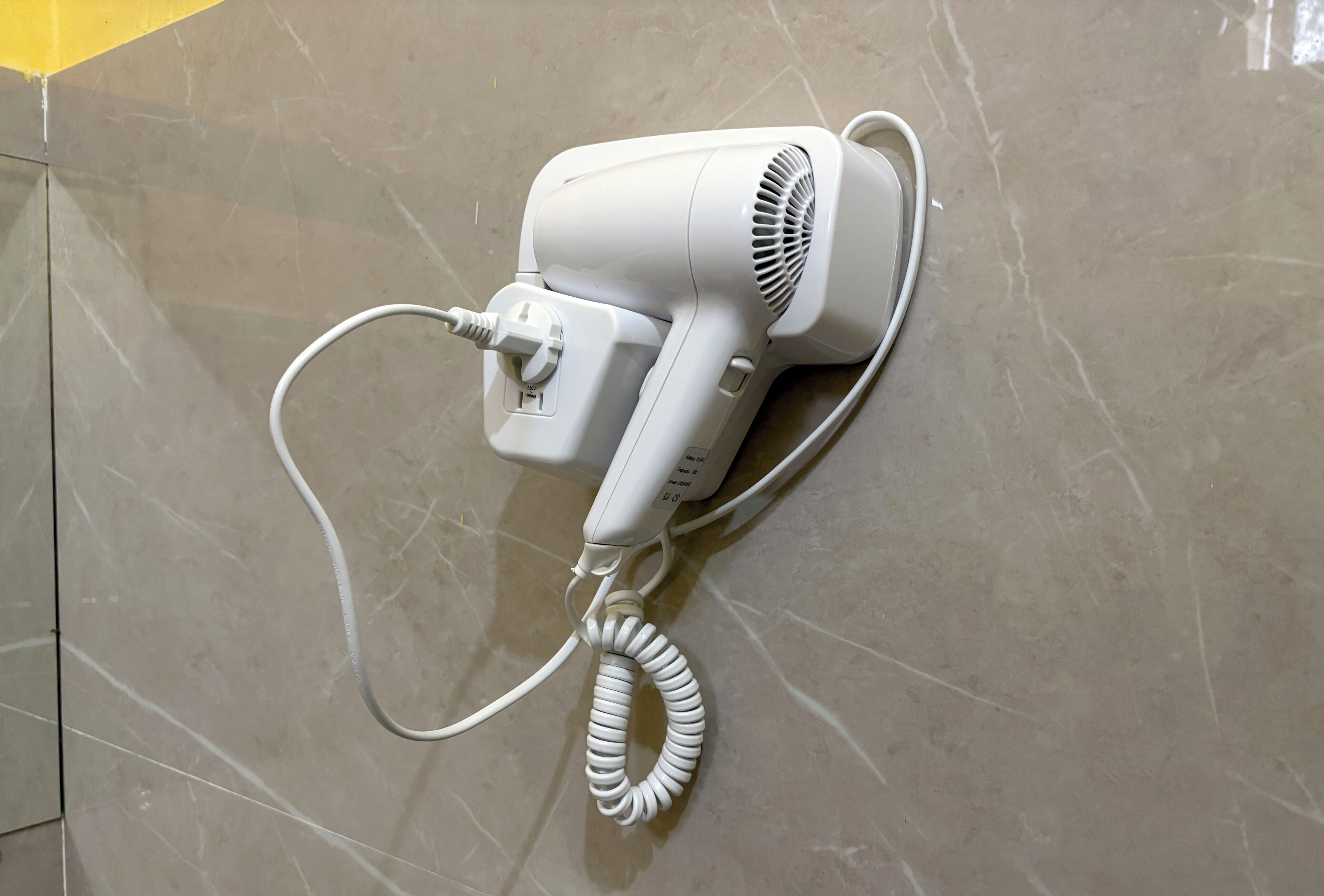 A white hair dryer mounted on a tiled wall.