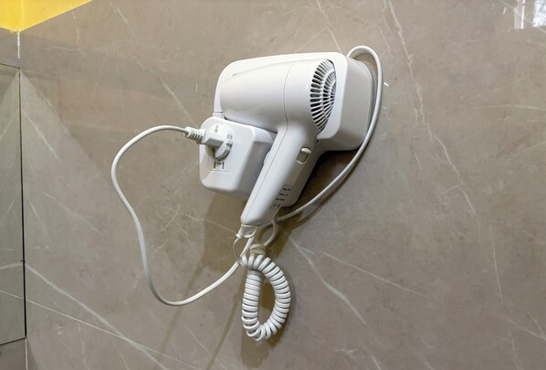 Un sèche-cheveux blanc fixé sur un mur recouvert de carreaux.