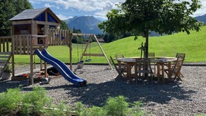 A playground with a slide, swings, and a wooden playhouse. - Gina's Apartment - Nähe zu See und Berge by Interhome (Sarnen)