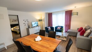 A modern living room with a wooden dining table, black chairs, a grey sofa, and a television on a cabinet. - Gina's Apartment - Nähe zu See und Berge by Interhome (Sarnen)