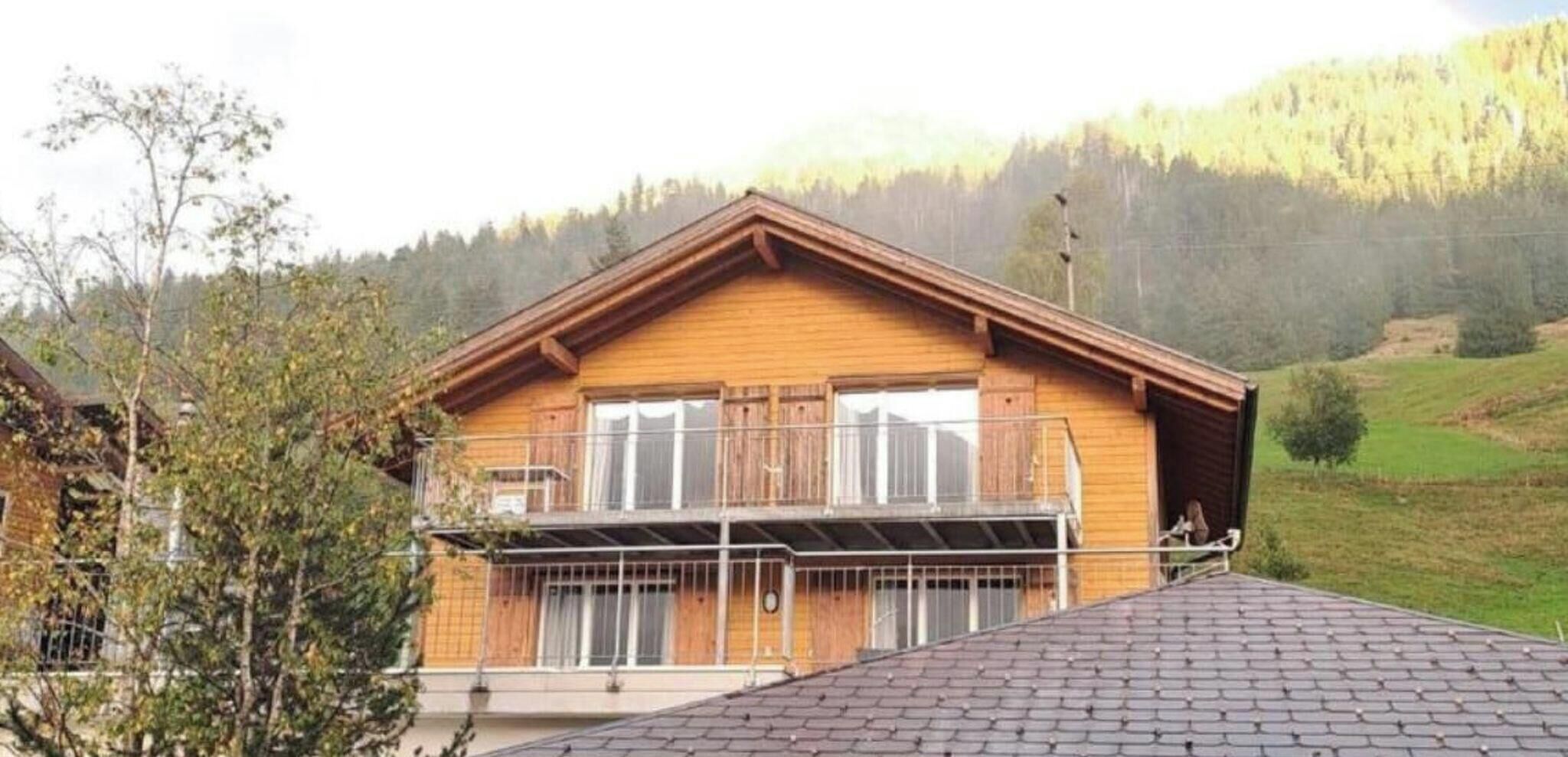 A wooden chalet with a balcony, set in a mountainous area.