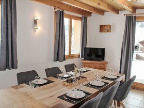 Ein Essbereich mit einem langen Holztisch, gedeckt für sechs Personen, einem Fernseher auf einem Holzboden und einem Fenster mit Vorhängen.