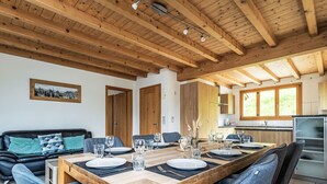 A dining area with a wooden table set for six, surrounded by blue chairs, a black leather sofa, and a kitchen in the background. - Stöckli auf dem Birkenhof mit Zusatzzimmer by Interhome (Sörenberg)