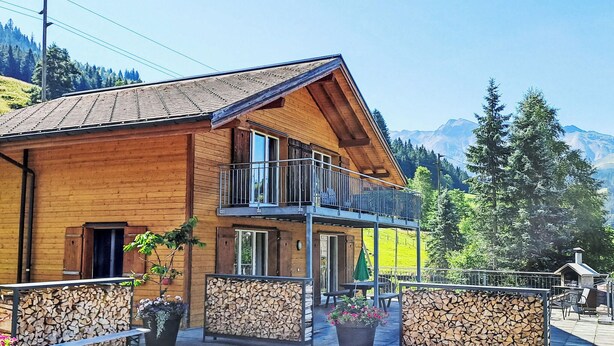 A wooden chalet with a balcony, a covered patio, and a mountain backdrop. - Stöckli auf dem Birkenhof mit Zusatzzimmer by Interhome (Sörenberg)
