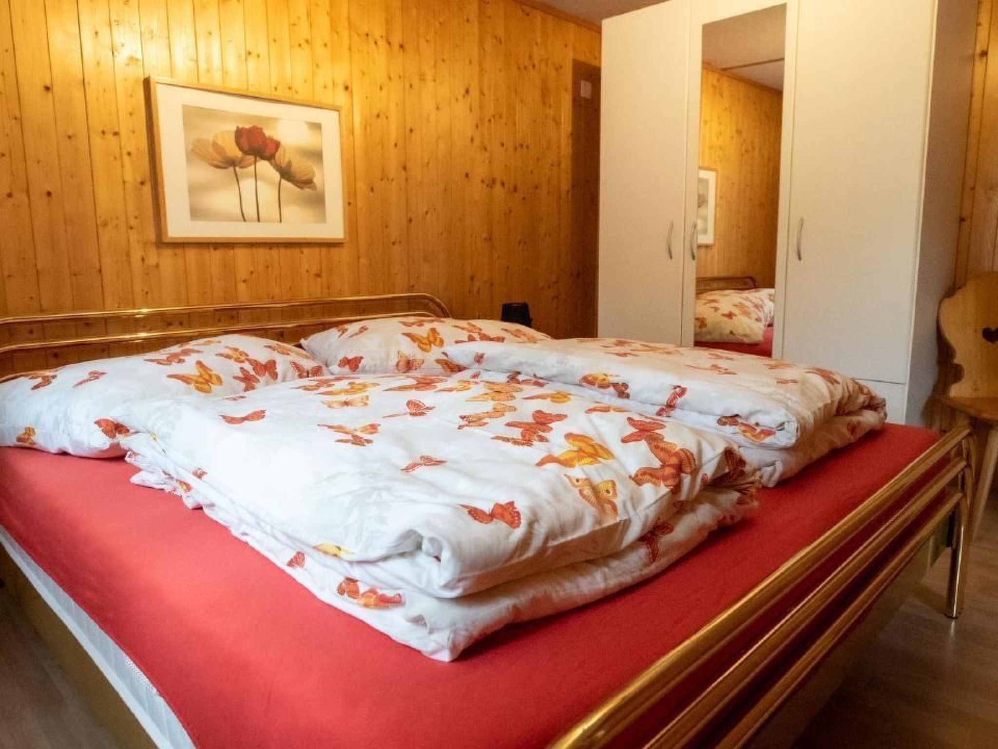 Ein Zimmer mit Holzwänden, einem Bett, einem gerahmten Bild an der Wand und einem Kleiderschrank.