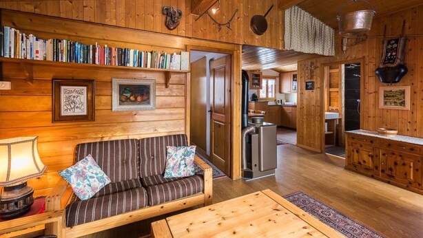 Ein gemütliches Blockhaus-Interieur mit einer Holzregal, einem gestreiften Sofa, einem Esstisch und einer Küchenzeile.
