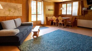 Un interior acogedor de cabaña con techo de madera, un sofá, una mesa de comedor con sillas y un televisor montado en la pared.