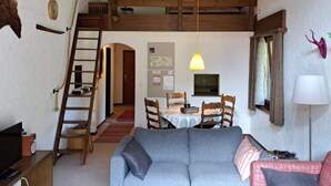 Una stanza in stile loft con un letto a soppalco, un tavolo da pranzo con sedie, un divano grigio, una TV e una lampada.