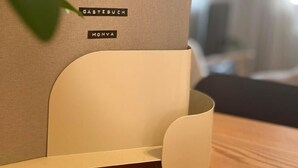 Un contenitore portaoggetti moderno e minimalista con le etichette 'GASTEBUCH' e 'MONYA'.