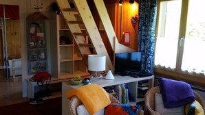Een knusse woonkamer met een houten trap, een televisie en rieten meubels.