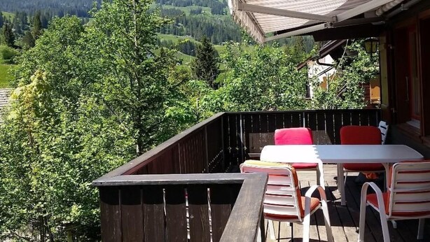 Een houten terras met zitplaatsen buiten en uitzicht op een bergachtig landschap.