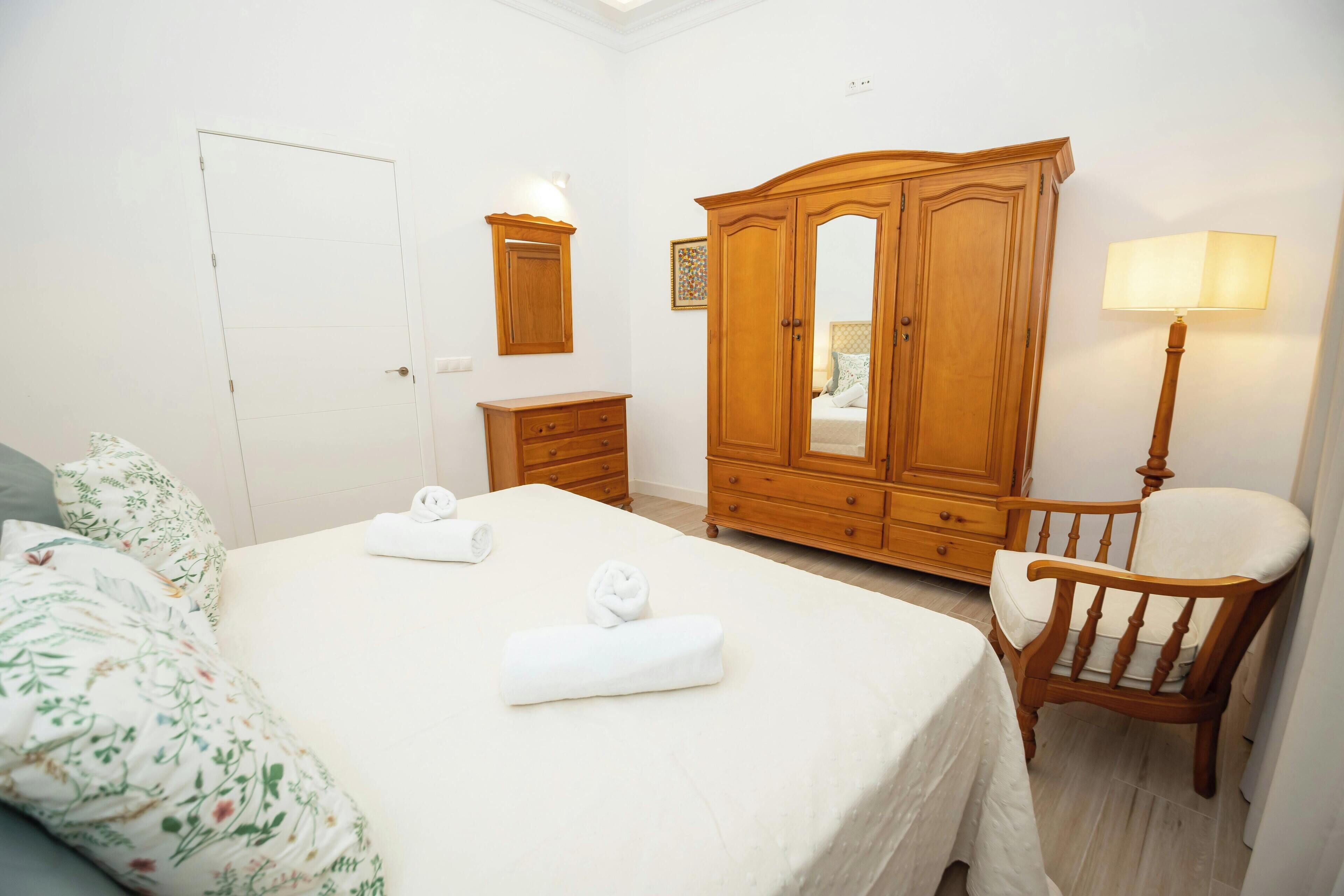 Een slaapkamer met een bed, een houten garderobe, een stoel, een nachtkastje en een lamp.