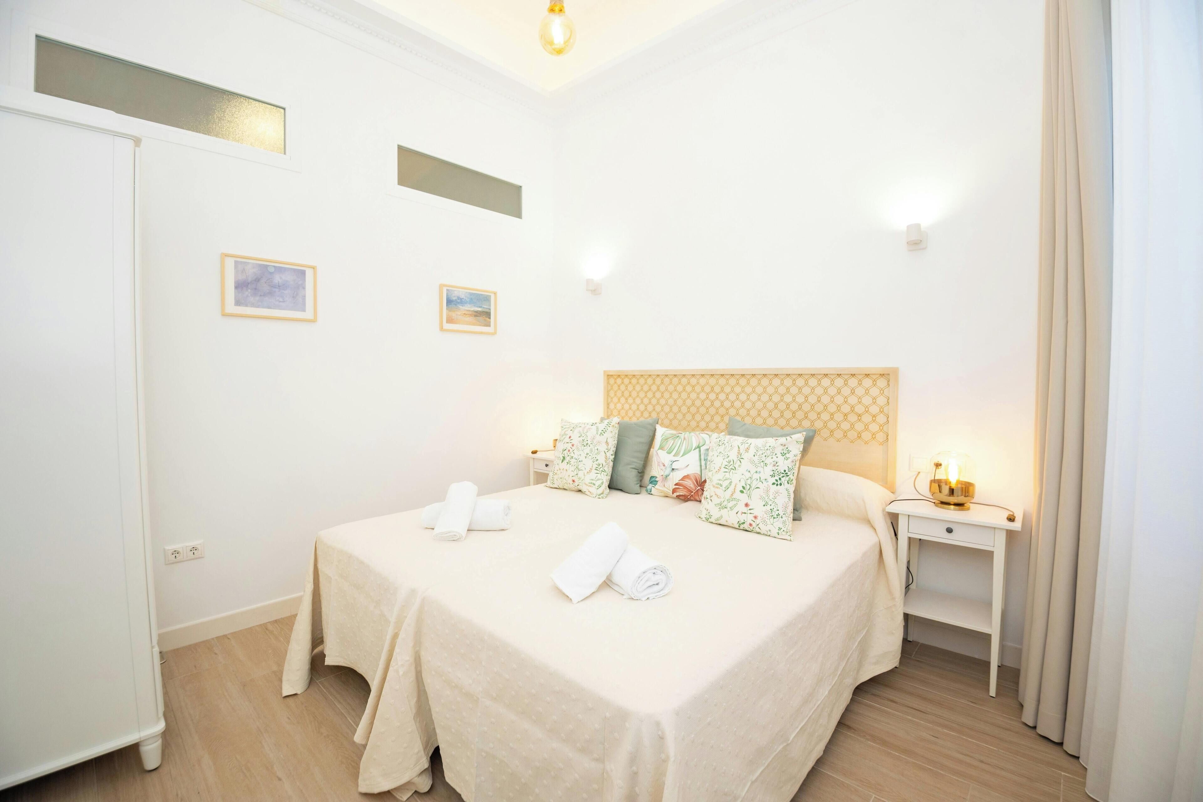 Una habitación de hotel con una cama, una mesita de noche y dos lámparas de pared.