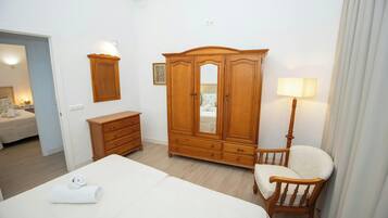 A hotel room with a large bed, a wooden wardrobe, a chair, a bedside table, and a lamp.