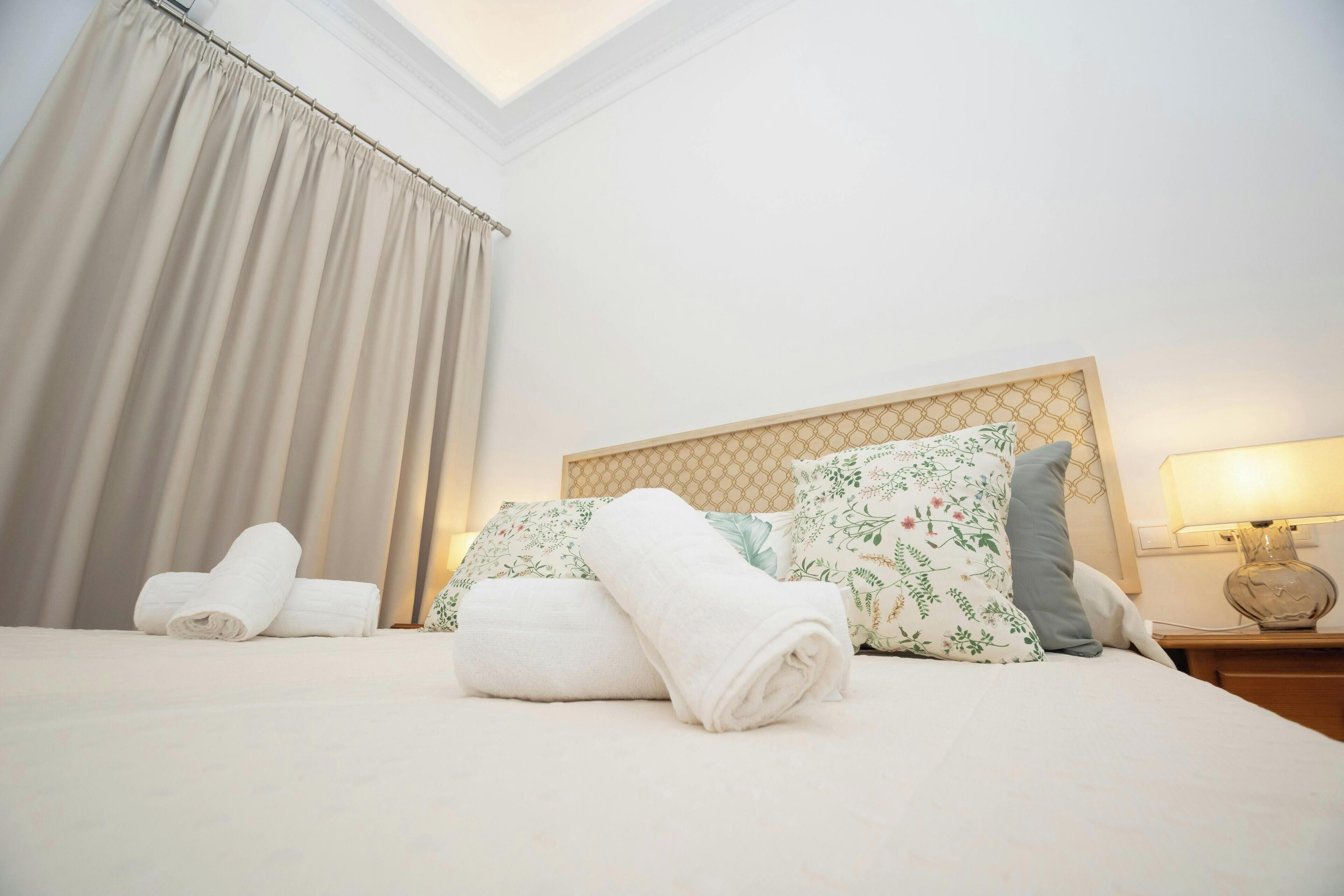 Un lit bien fait, avec des serviettes pliées, des coussins à motifs floraux et une tête de lit ornée d’un motif géométrique.