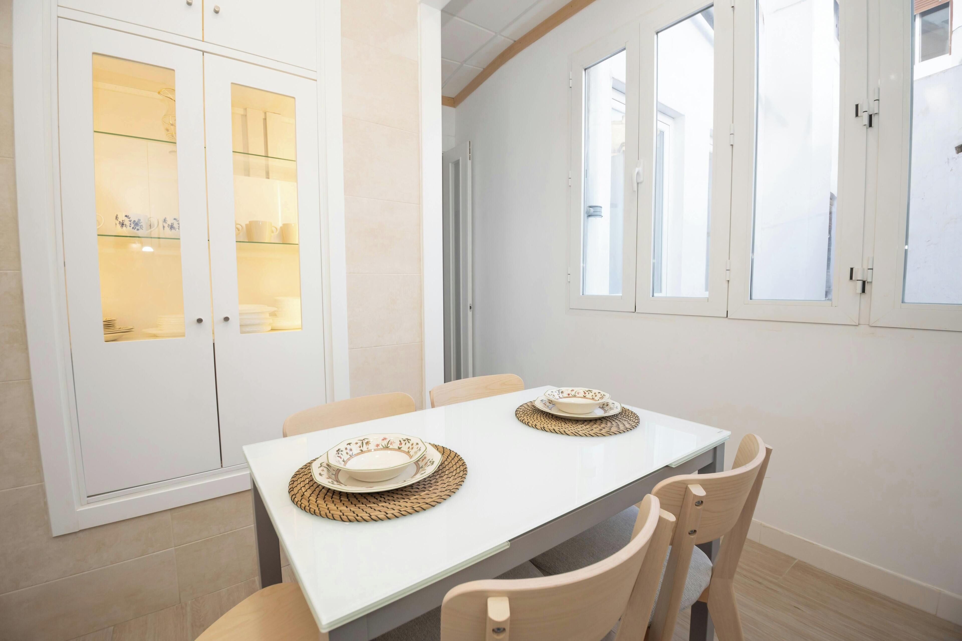Un comedor con una mesa blanca, dos sillas y un mueble con puertas de vidrio.