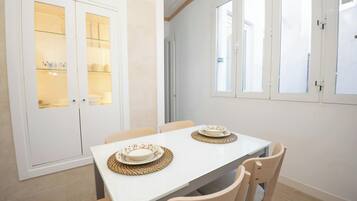 Un comedor con una mesa blanca, dos sillas y un mueble con puertas de vidrio.