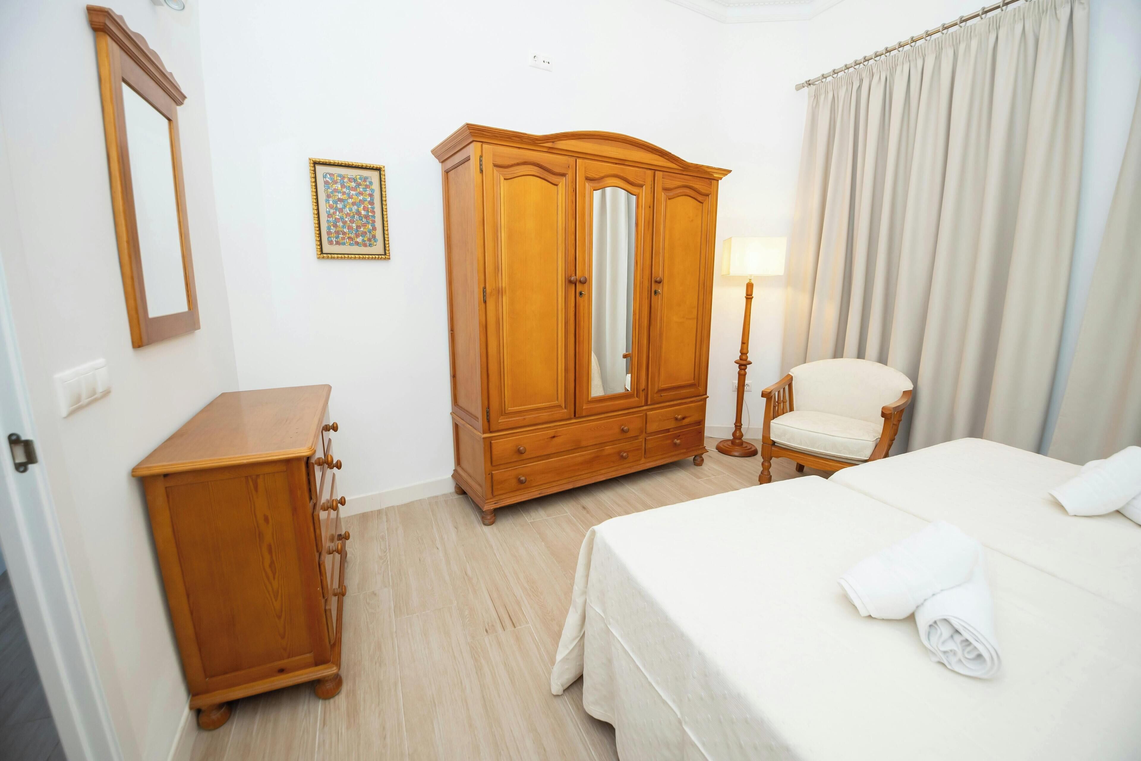 Una habitación de hotel con una cama, un armario de madera, una silla y una lámpara.