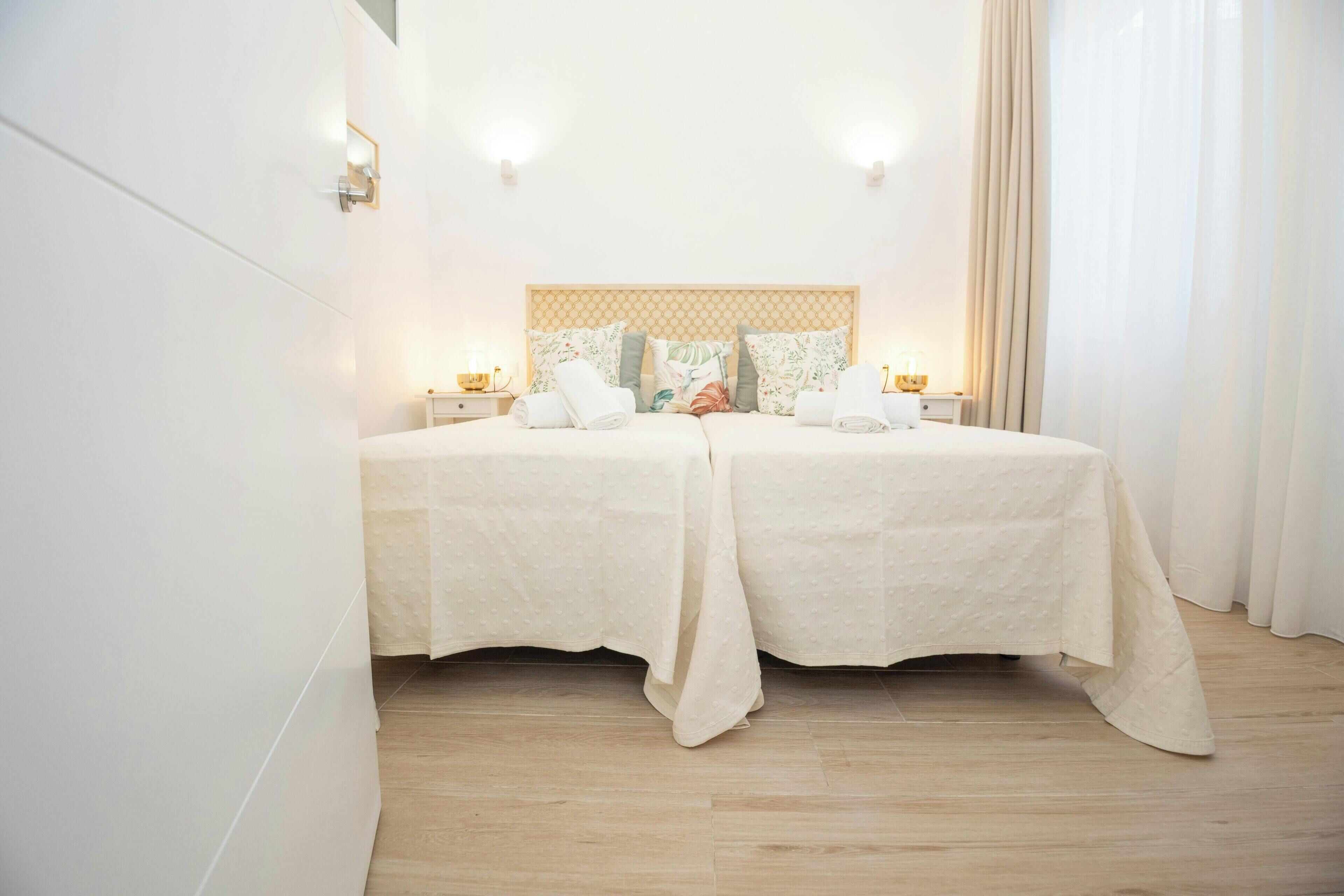 A double bed with a beige headboard, two bedside tables with lamps, and a light-colored floor.