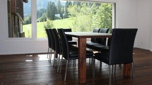 Un comedor con una mesa de madera y sillas negras, ventanas amplias con vistas a un paisaje verde.