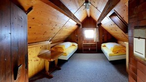 Un pequeño y acogedor dormitorio en el ático, con paredes de madera y techo inclinado. Hay dos camas individuales con ropa de cama amarilla y una pequeña mesa de madera.