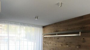 Una habitación moderna con un panel de madera decorativo, un banco oscuro y un ventanal con cortinas translúcidas.