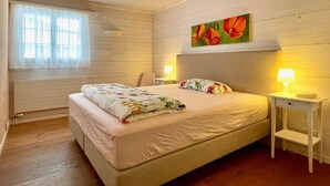 Een slaapkamer met een groot bed, een stoel, een nachtkastje met een lamp en een raam met gordijnen.
