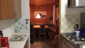 A kitchen with wooden cabinets, a red coffee machine, a dining area with a table and chairs, and a tiled backsplash.