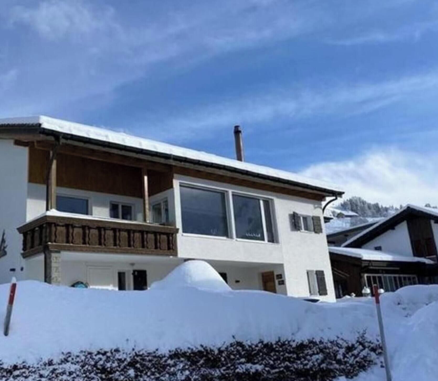 Ein zweistöckiges Gebäude mit Balkon, großen Fenstern und einem mit Schnee bedeckten Dach.