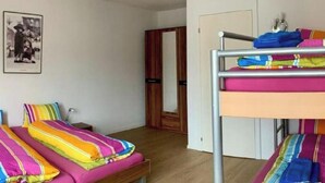 Ein Schlafsaalzimmer mit Etagenbetten, einem kleinen Nachttisch, einer Lampe und einem gerahmten Bild an der Wand.
