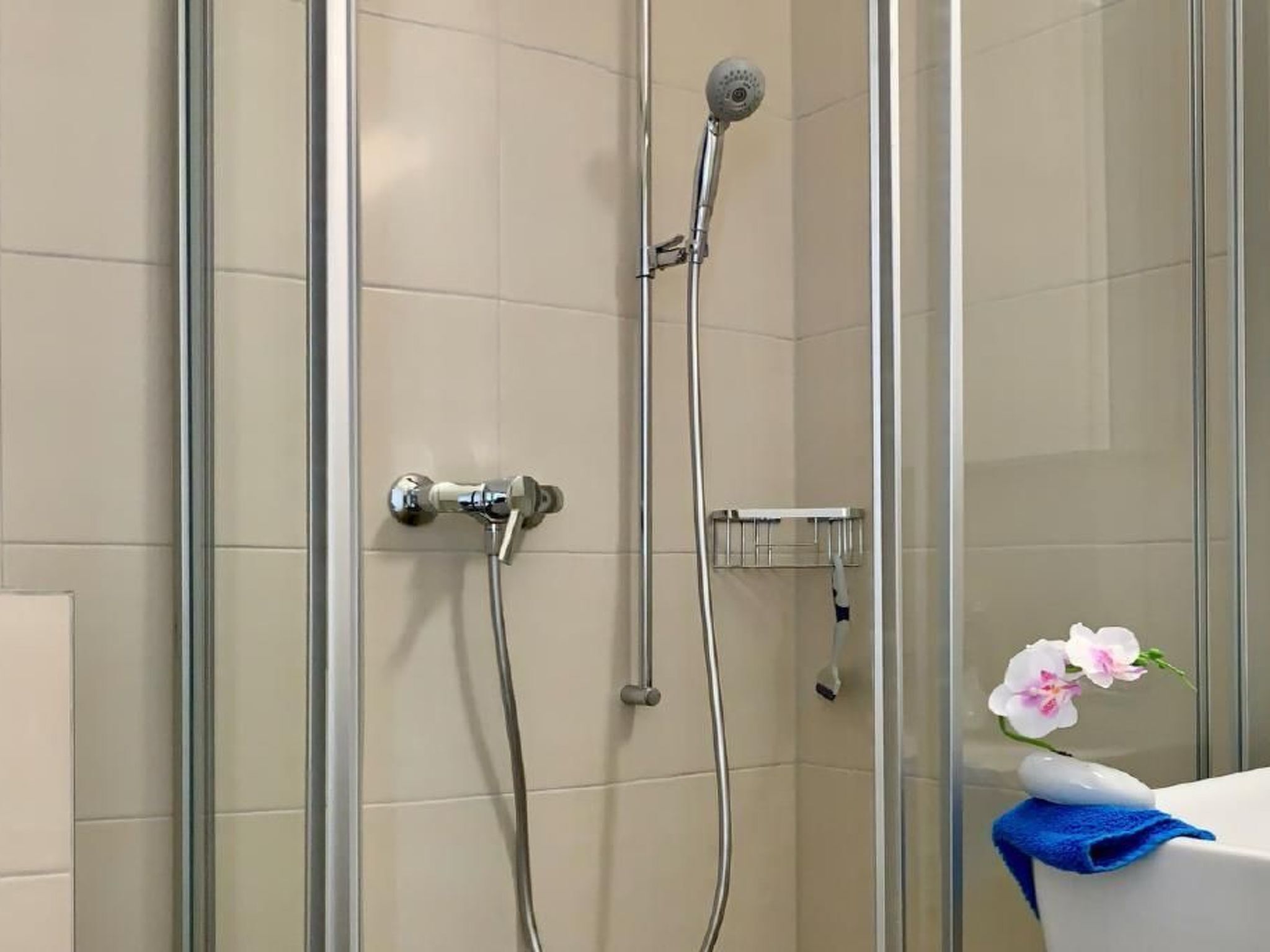 Cabina doccia in vetro con soffione a mano e rubinetto a parete.