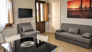 Un soggiorno con un tavolo da pranzo nero, due divani grigi, una TV a parete e un dipinto del tramonto.