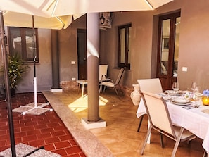 Un espace de restauration en plein air avec une table dressée pour deux personnes, une plante en pot et un sol en briques.