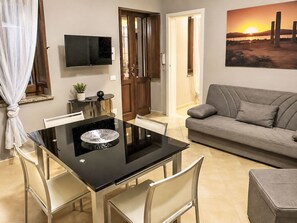 Ein modernes Wohnzimmer mit Esstisch, Sofa, Fernseher und einem Sonnenuntergangsbild.