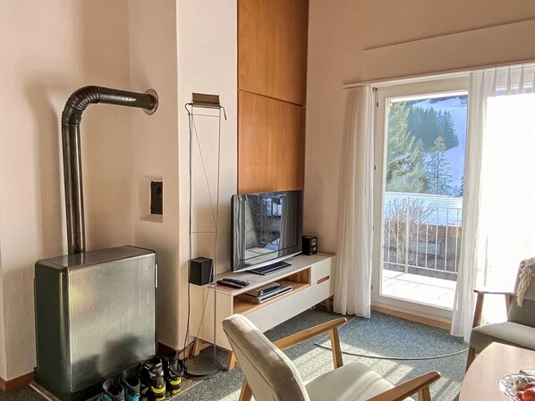 A hotel room with a television, a small table, a chair, a shoe rack, and a view of the outdoors. - Haus Reanchme by Interhome (Sörenberg)