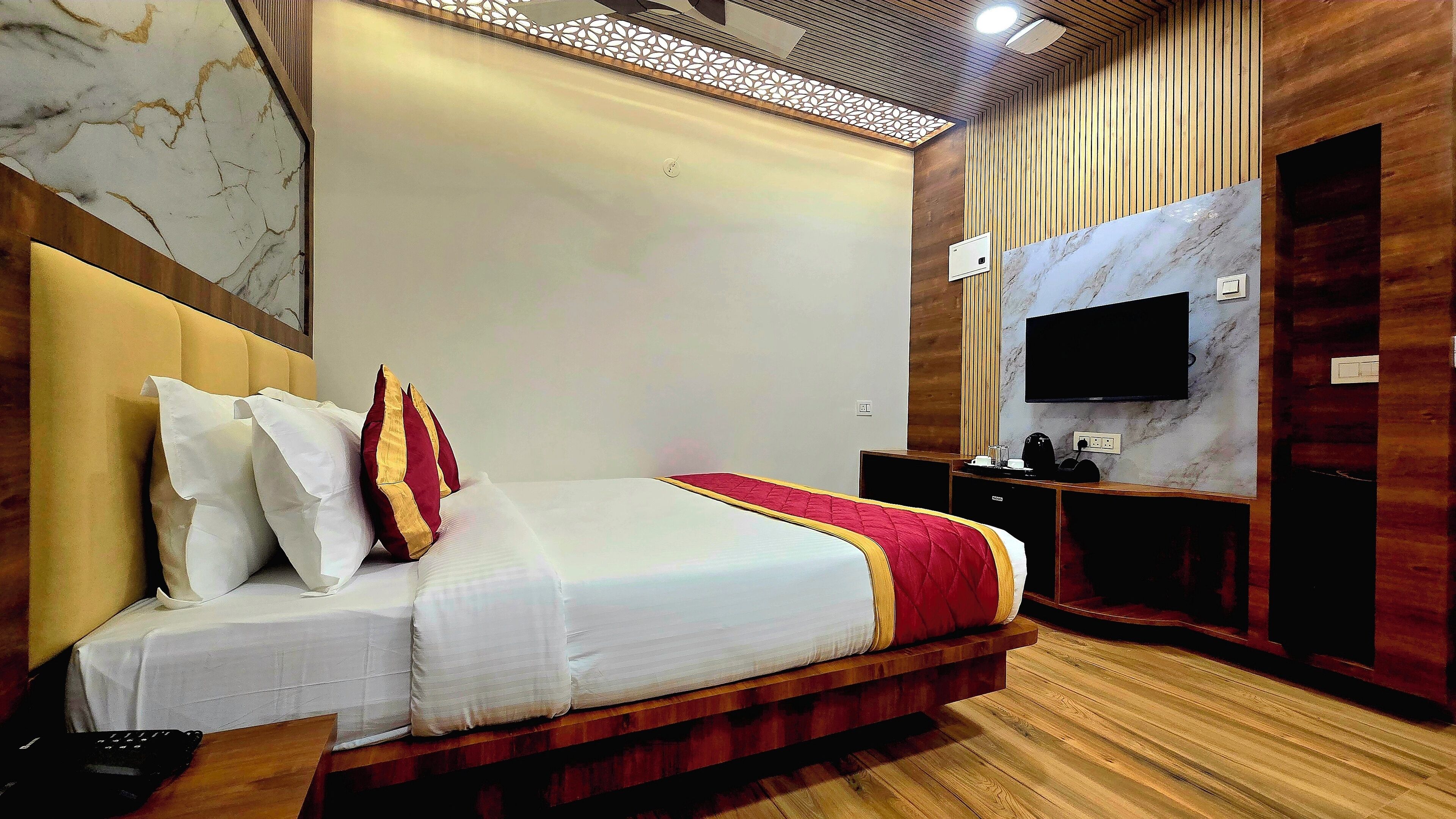 A modern hotel room with a large bed, wooden paneling, a flat-screen TV, and a marble accent wall.